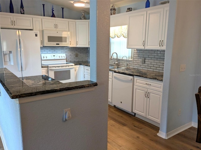 kitchen with white appliances, a kitchen island, white cabinets, dark stone counters, and wood finished floors