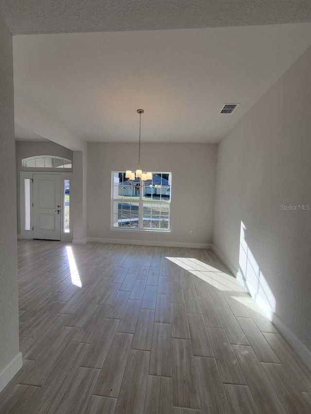 unfurnished dining area with wood tiled floor, a wealth of natural light, baseboards, and a chandelier