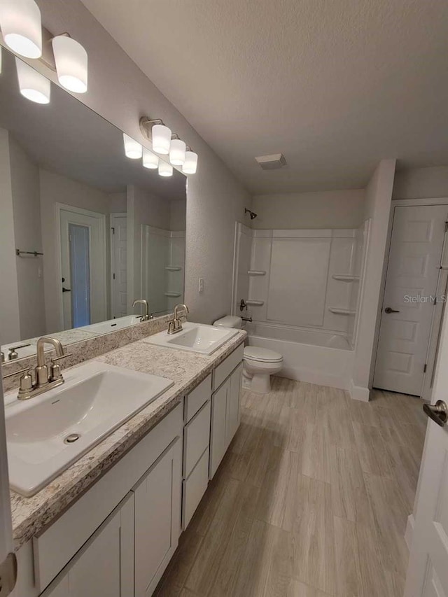 full bathroom with toilet, a sink, a textured ceiling, and wood finished floors
