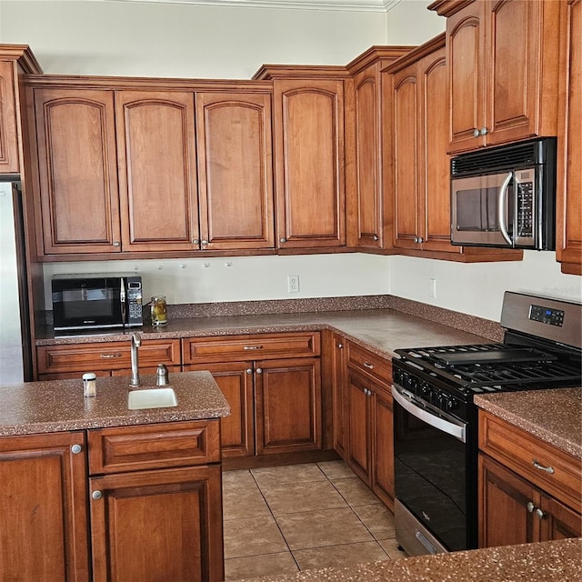 kitchen with brown cabinets, dark stone counters, appliances with stainless steel finishes, a sink, and light tile patterned floors