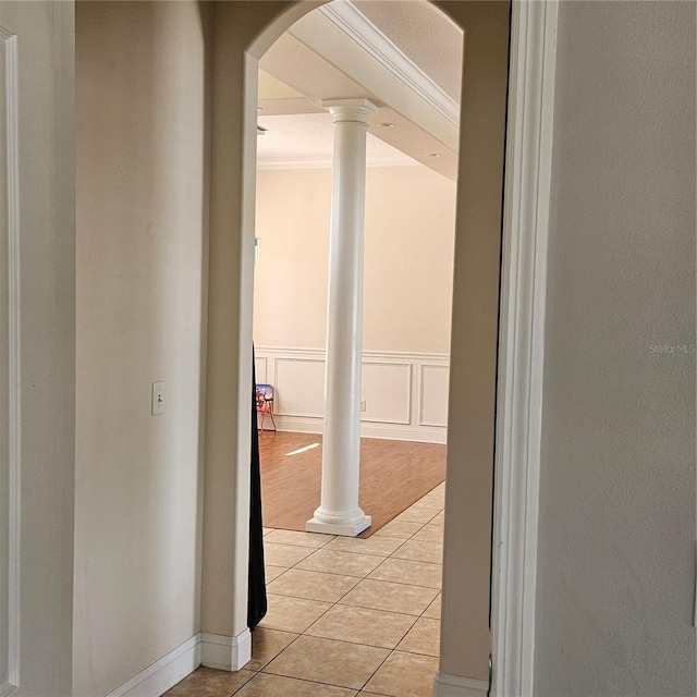 corridor featuring crown molding, ornate columns, light tile patterned flooring, arched walkways, and a decorative wall