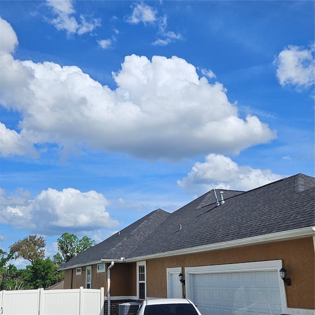 view of property exterior with stucco siding, an attached garage, fence, and roof with shingles