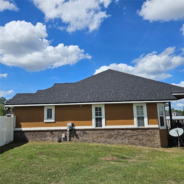 rear view of property with a shingled roof, a lawn, stucco siding, and fence