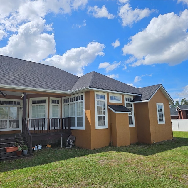 rear view of property with stucco siding, a shingled roof, a porch, and a yard