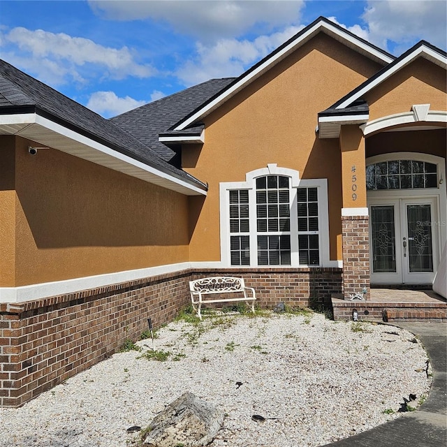 exterior space featuring french doors, brick siding, stucco siding, and roof with shingles
