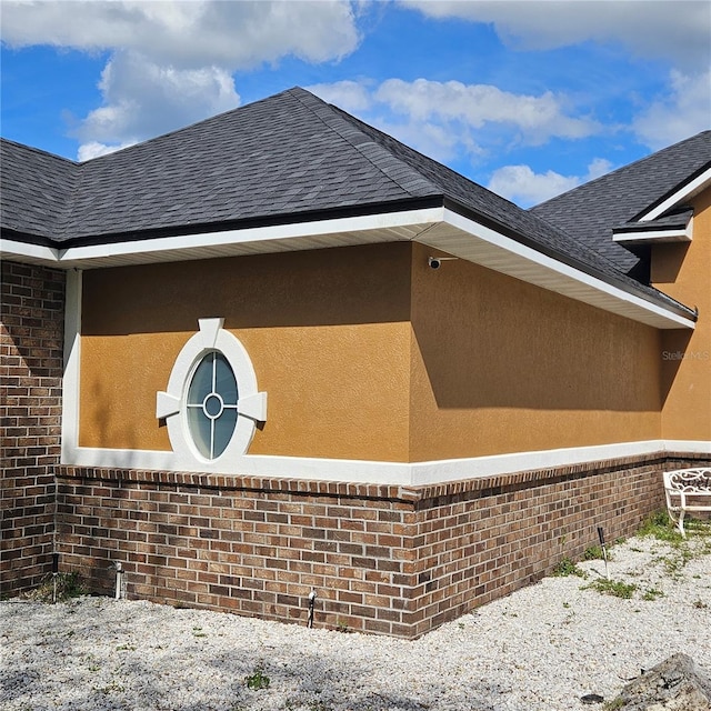 view of side of property with brick siding, stucco siding, and roof with shingles