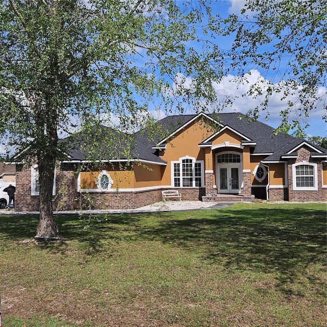 view of front of property featuring french doors, brick siding, a front yard, and stucco siding