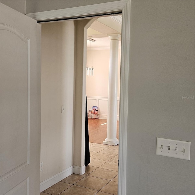 hallway with a wainscoted wall, a decorative wall, light tile patterned floors, arched walkways, and ornate columns