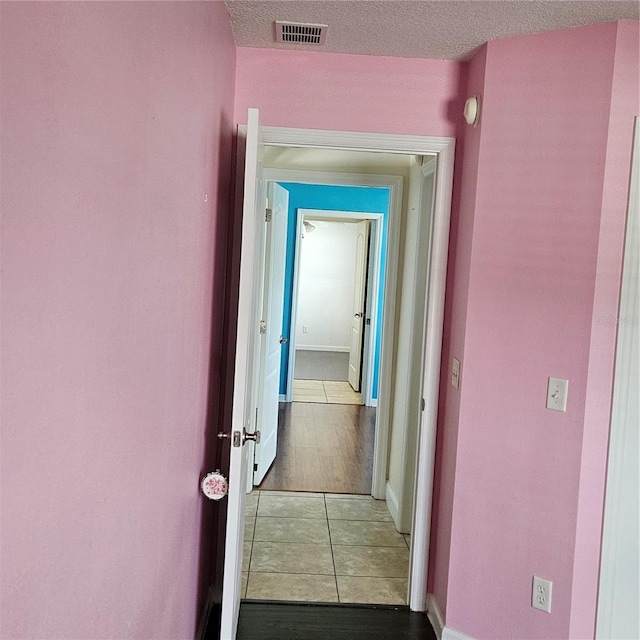 hall with tile patterned floors, visible vents, baseboards, and a textured ceiling