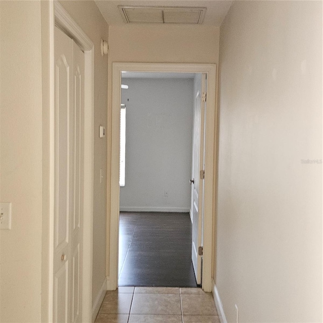 hallway featuring attic access, light tile patterned flooring, baseboards, and visible vents
