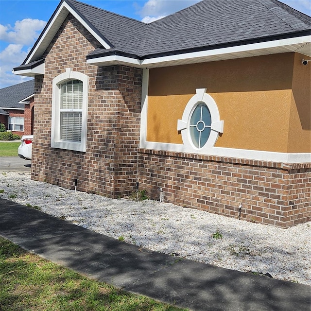 view of home's exterior with brick siding, a shingled roof, and stucco siding