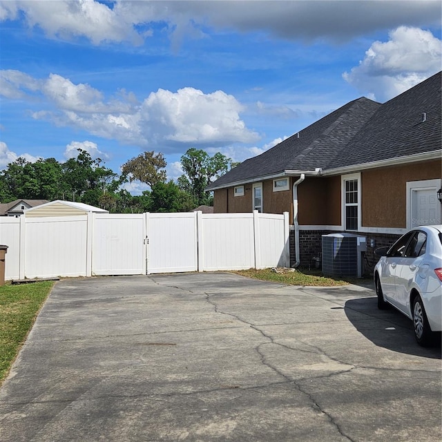 view of side of home with a gate, roof with shingles, stucco siding, fence, and central AC unit