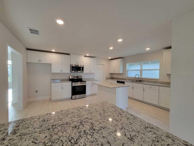 9553 SW 42nd Ave, Ocala, FL 34476 - kitchen with stainless steel appliances, a sink, light wood-style floors, white cabinetry, and light stone countertops