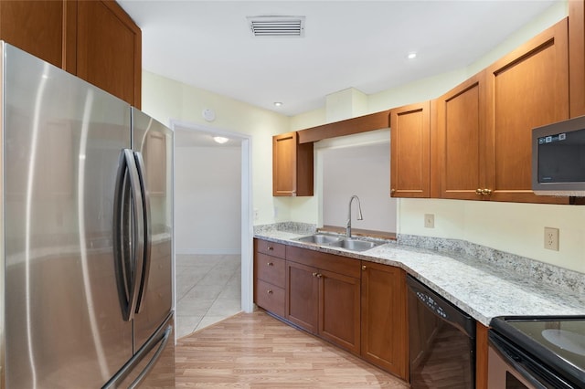 kitchen featuring visible vents, light stone counters, a sink, stainless steel appliances, and brown cabinets