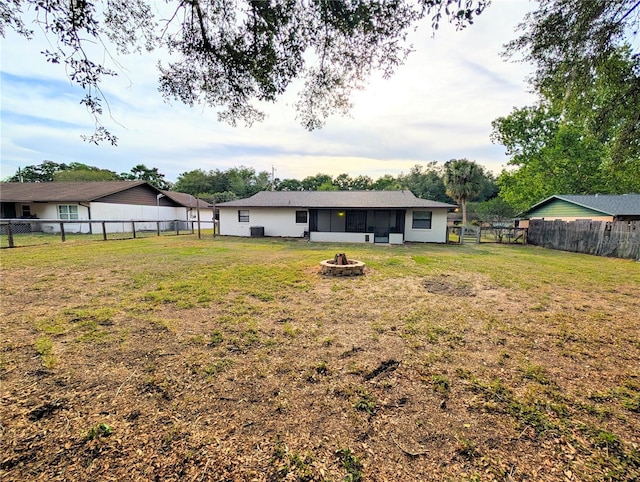 rear view of house with a yard, a fenced backyard, and an outdoor fire pit