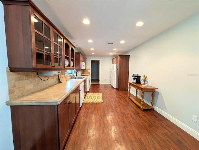kitchen with decorative backsplash, white appliances, light countertops, baseboards, and dark wood-style flooring