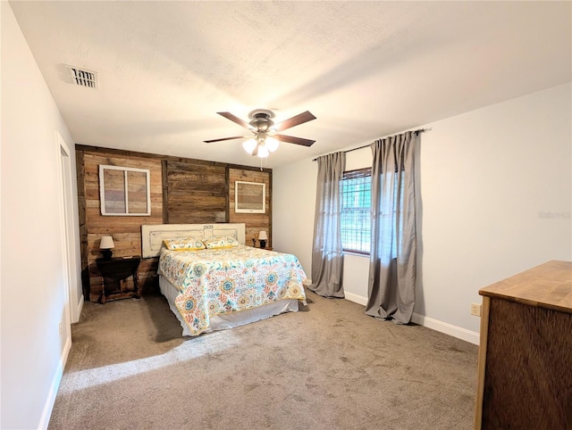 carpeted bedroom with baseboards, wooden walls, visible vents, and a ceiling fan