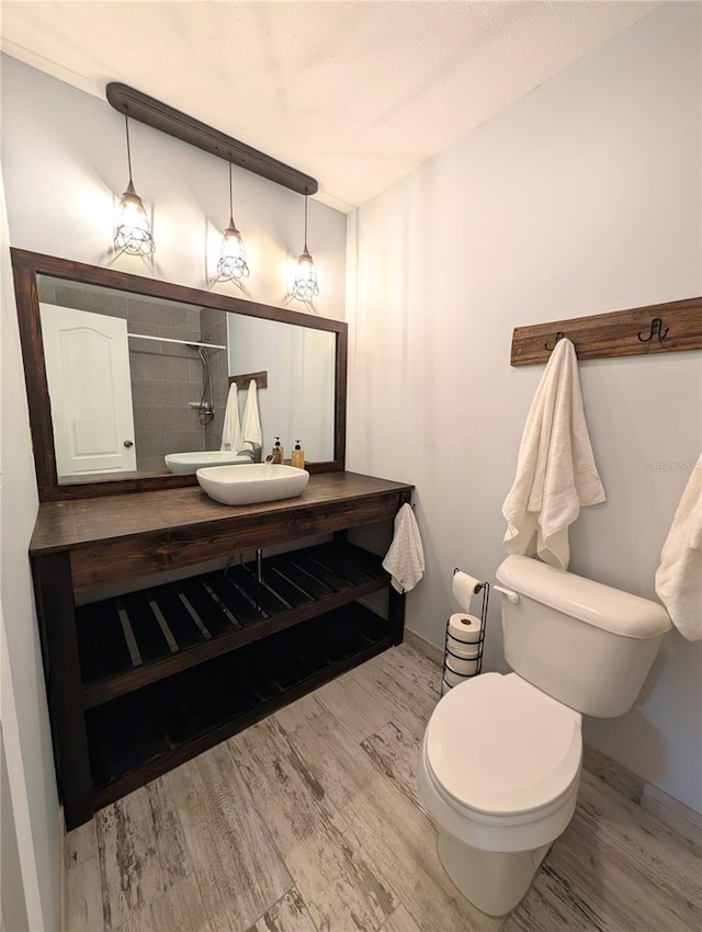 bathroom featuring wood finished floors, vanity, a shower, baseboards, and toilet