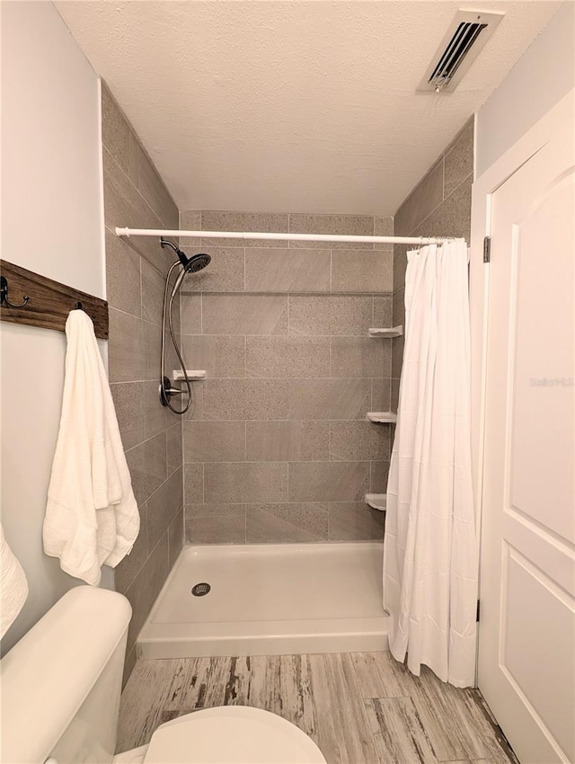 bathroom featuring a stall shower, wood finished floors, visible vents, and toilet