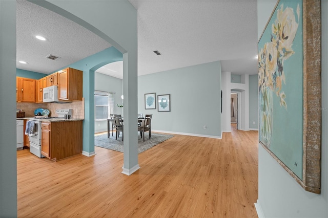 kitchen featuring arched walkways, a textured ceiling, light wood finished floors, and white appliances