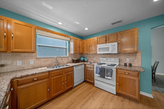 kitchen with a sink, a textured ceiling, light wood-type flooring, backsplash, and white appliances