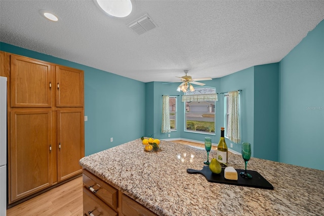 kitchen with light wood-style flooring, visible vents, light stone countertops, and brown cabinetry