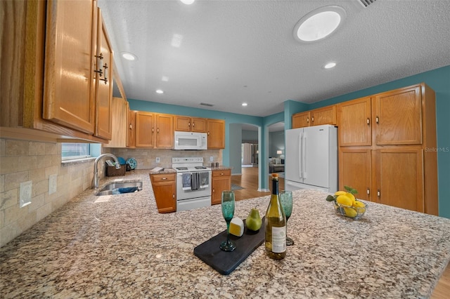 kitchen featuring arched walkways, a sink, backsplash, white appliances, and light stone countertops