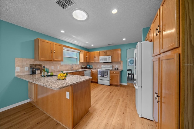 kitchen with visible vents, a sink, white appliances, decorative backsplash, and a peninsula