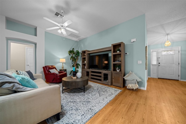 living area with vaulted ceiling, ceiling fan, light wood finished floors, baseboards, and visible vents