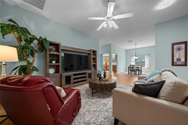 living room with arched walkways, wood finished floors, visible vents, and ceiling fan