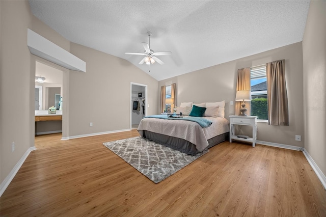 bedroom with vaulted ceiling, wood finished floors, a textured ceiling, ensuite bathroom, and baseboards