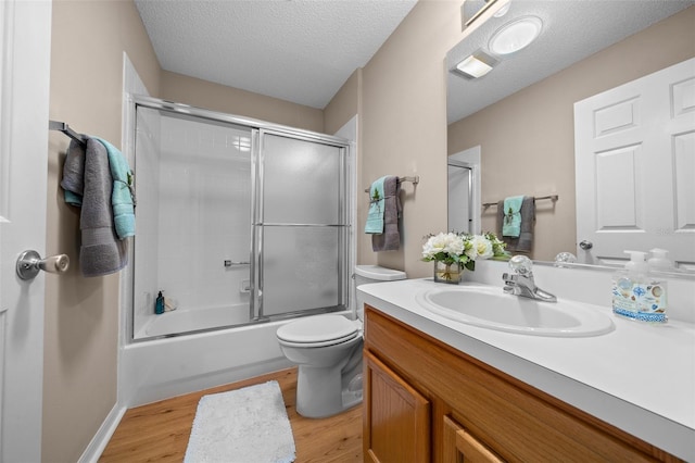 bathroom featuring wood finished floors, a textured ceiling, vanity, toilet, and shower / bath combination with glass door