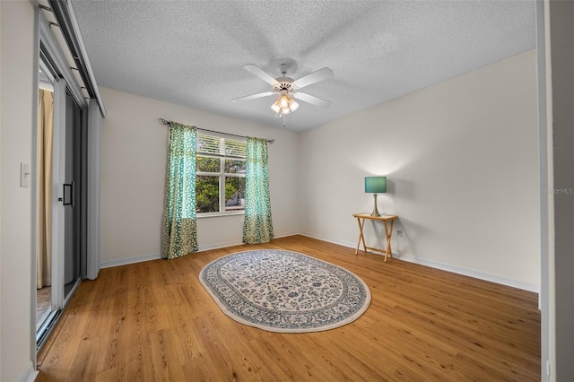 spare room featuring baseboards, a ceiling fan, wood finished floors, and a textured ceiling