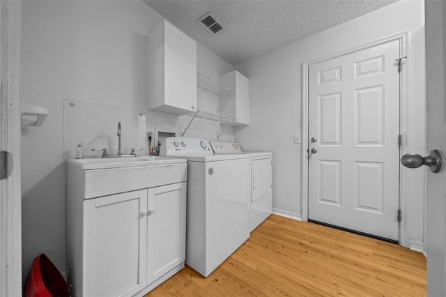 laundry room with a sink, light wood-style floors, washing machine and clothes dryer, cabinet space, and a textured ceiling
