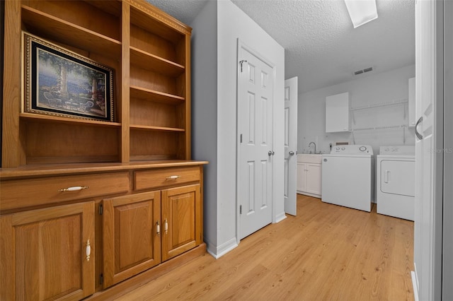 clothes washing area with cabinet space, light wood finished floors, visible vents, and independent washer and dryer