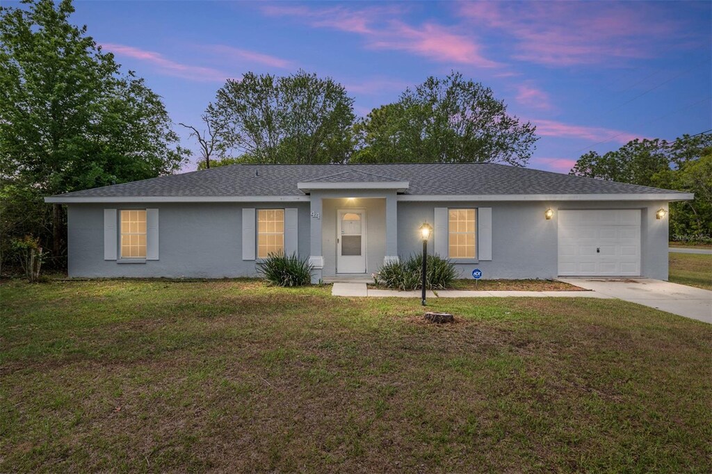 44 Pecan Run Dr, Ocala, FL 34472 - ranch-style house with an attached garage, concrete driveway, a front lawn, stucco siding, and roof with shingles