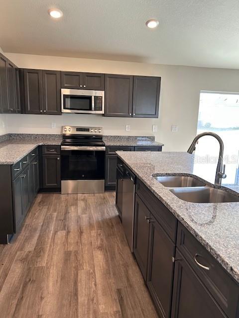 kitchen with a sink, appliances with stainless steel finishes, recessed lighting, wood finished floors, and light stone countertops