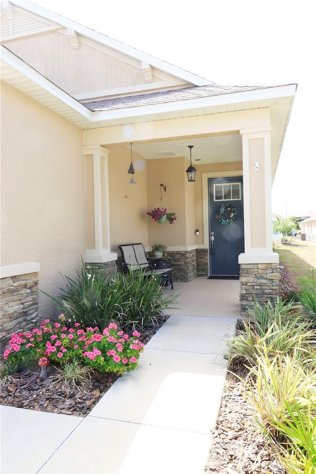 view of exterior entry featuring covered porch, stucco siding, and stone siding