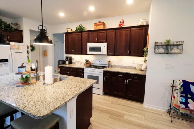 kitchen with a kitchen breakfast bar, light stone counters, a sink, light wood-style floors, and white appliances