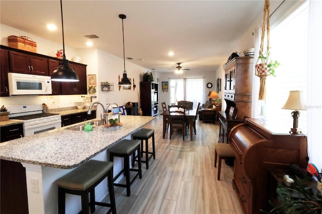 kitchen with white appliances, a kitchen island with sink, a breakfast bar area, a sink, and visible vents