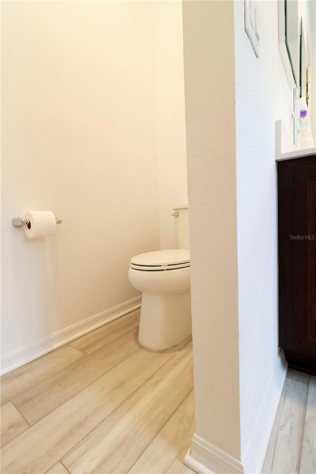 half bathroom with baseboards, wood finished floors, toilet, and vanity