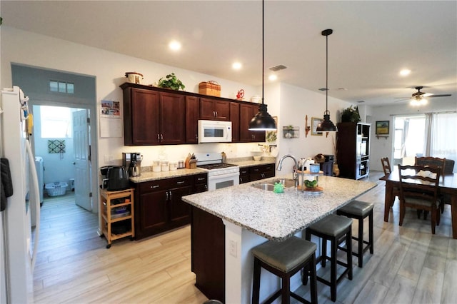 kitchen featuring a sink, dark brown cabinets, a kitchen bar, light wood-type flooring, and white appliances
