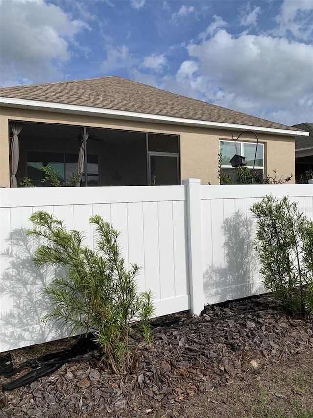 view of home's exterior featuring fence, roof with shingles, and stucco siding