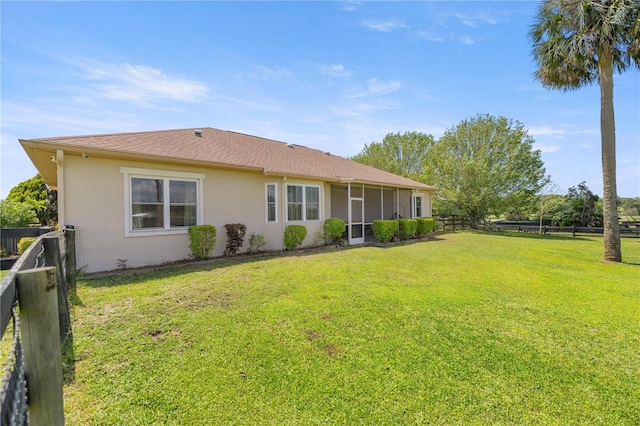 rear view of property with stucco siding, a fenced backyard, a sunroom, and a lawn