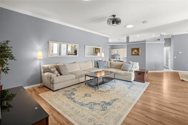living room with ornamental molding, visible vents, baseboards, and wood finished floors