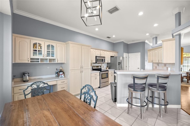 kitchen with light tile patterned floors, a kitchen bar, a peninsula, cream cabinetry, and stainless steel appliances