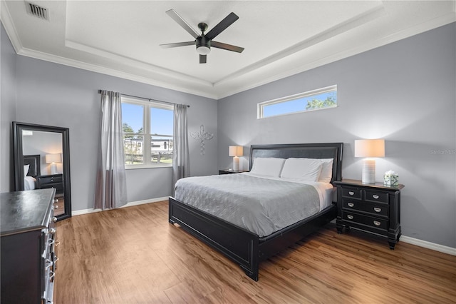 bedroom featuring visible vents, a tray ceiling, baseboards, and wood finished floors