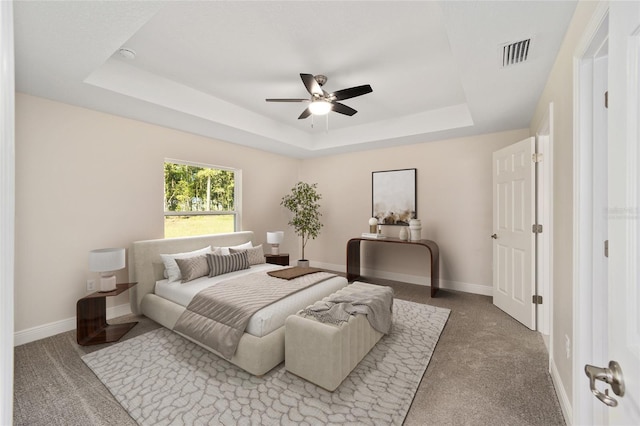 carpeted bedroom with ceiling fan, baseboards, a tray ceiling, and visible vents