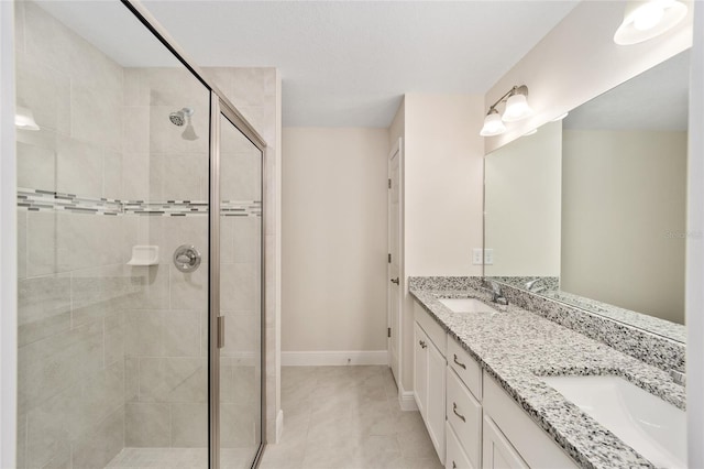 bathroom featuring double vanity, a shower stall, baseboards, and a sink