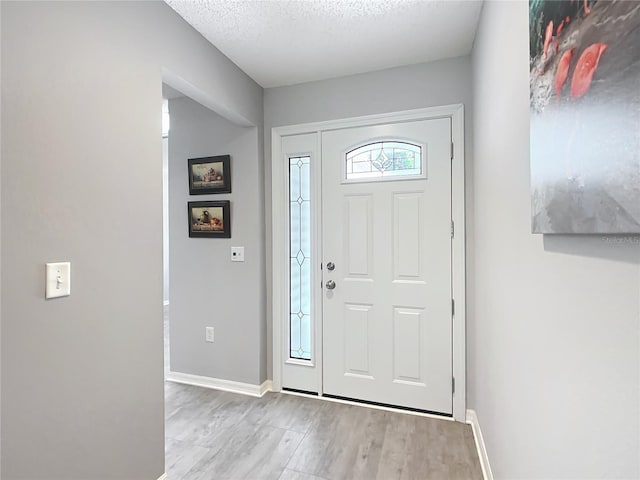 entrance foyer featuring a textured ceiling, baseboards, and light wood finished floors